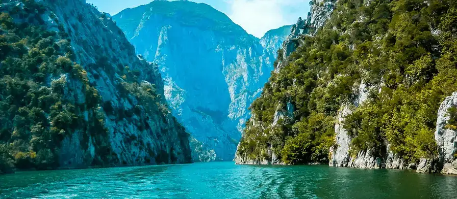 A small boat on Komani Lake beneath the canyon walls
