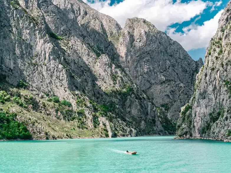 Two sea kayaks on the flat green water of Komani Lake beneath high canyon walls