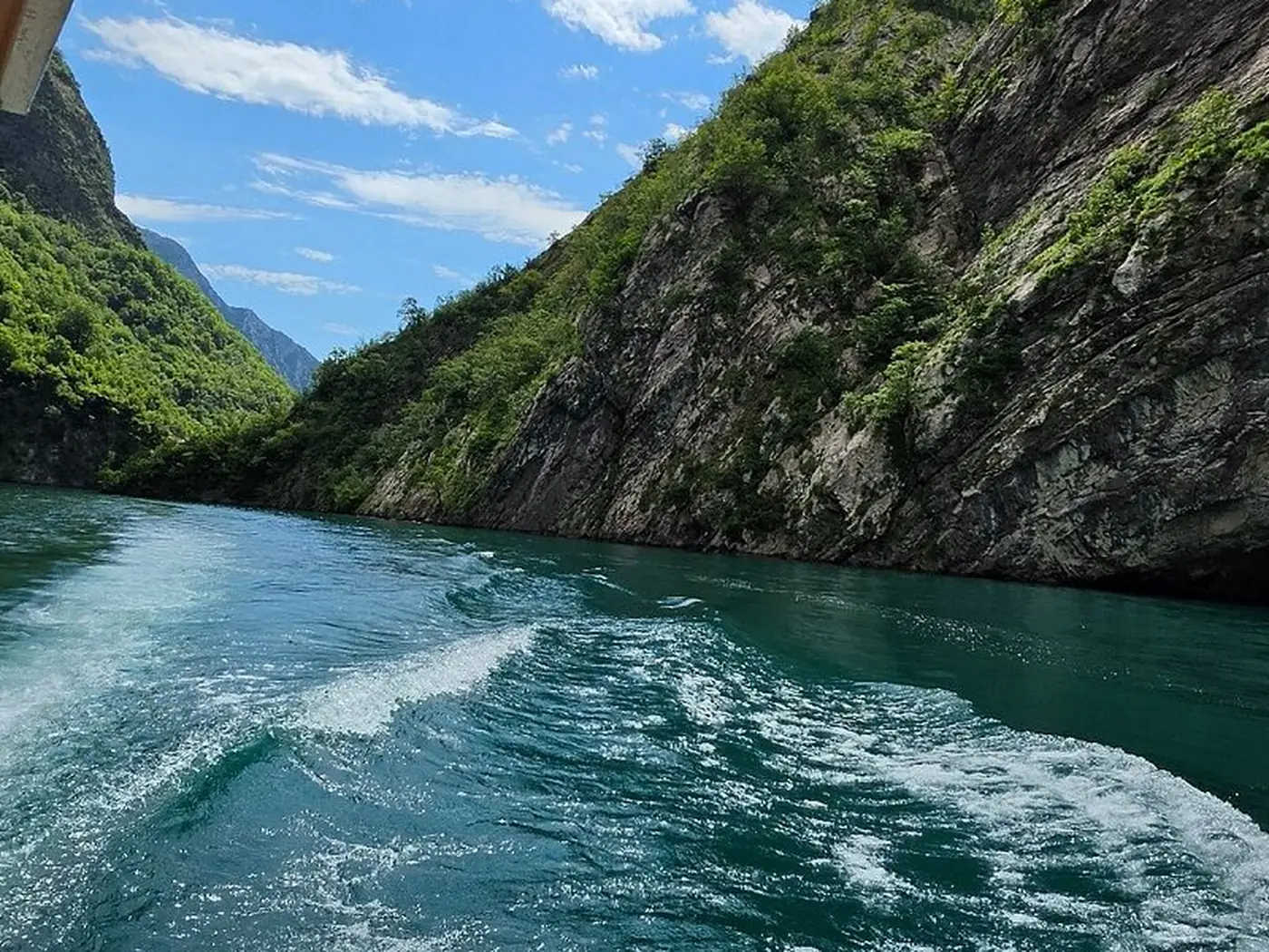 Two sea kayaks on the flat green water of Komani Lake beneath high canyon walls